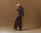 Man in dark outfit walking on a brown background wearing Triple Obsidian Gobi Sneaker II Premium Leather by Vivobarefoot